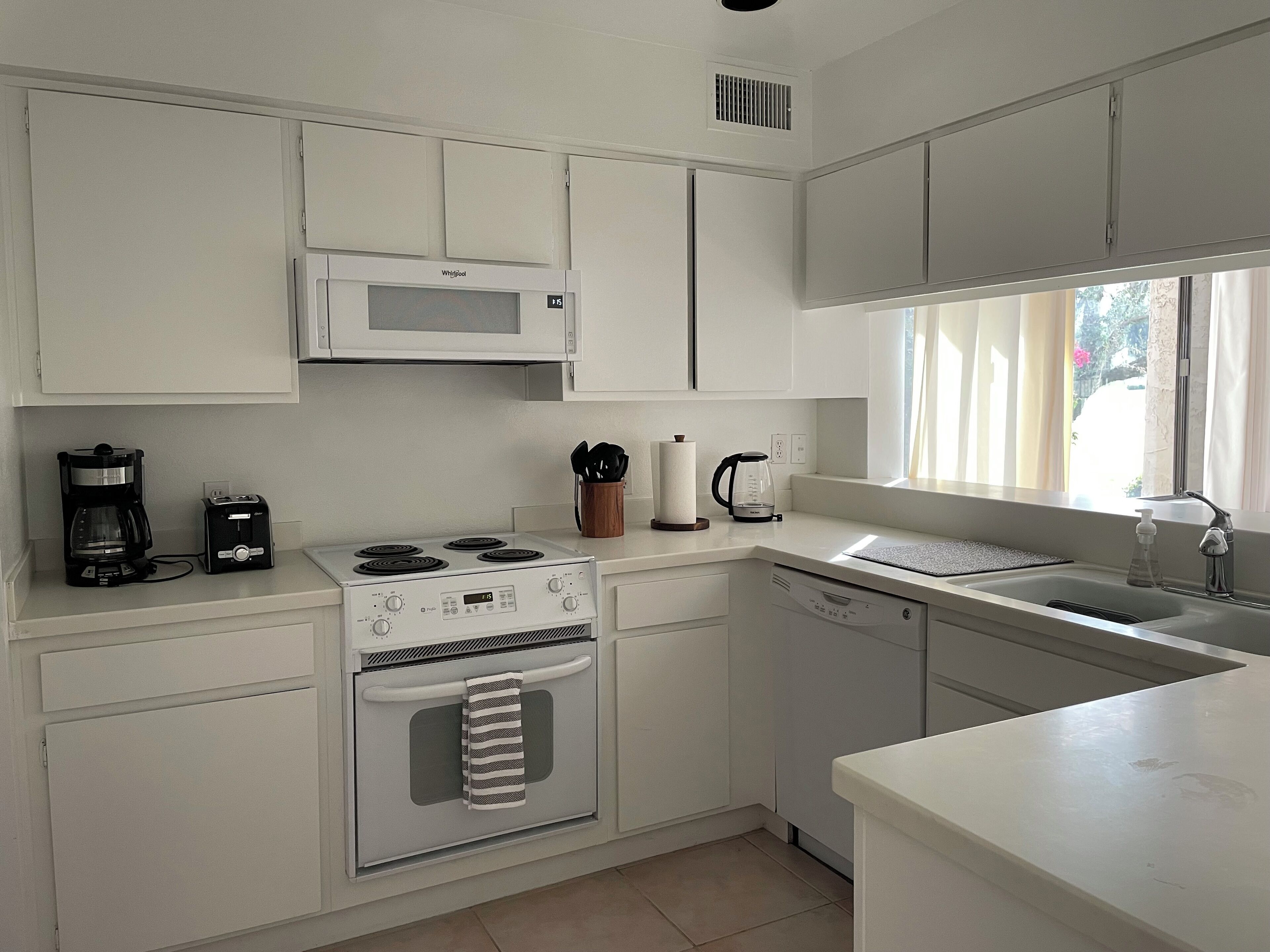 A modern kitchen with white cabinets, a microwave, a stove, a coffee maker, and a dishwasher.