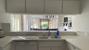 A modern kitchen with white cabinetry, a built-in dishwasher, a sink with a faucet, and a window overlooking a garden. - Quiet, comfortable 2-bedroom condo at Mission Hills in Rancho Mirage (Rancho Mirage)