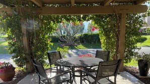 A covered patio with a round table and four chairs, surrounded by greenery and flowering plants. - Quiet, comfortable 2-bedroom condo at Mission Hills in Rancho Mirage (Rancho Mirage)