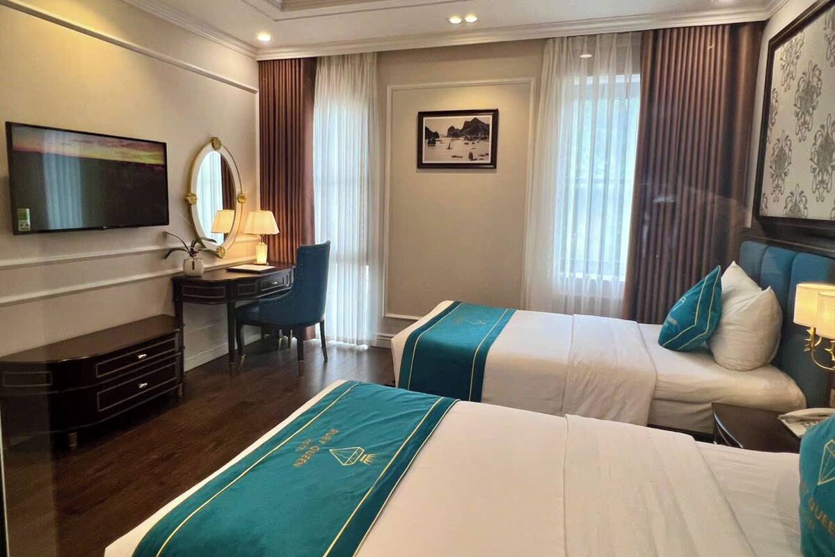 A hotel room with two beds, a desk, a chair, a TV, and a framed picture on the wall.