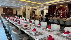 A long dining table set with white plates, red napkins, and clear glasses, surrounded by chairs with beige cushions. - Ruby Queen Hotel (Bai Chay)