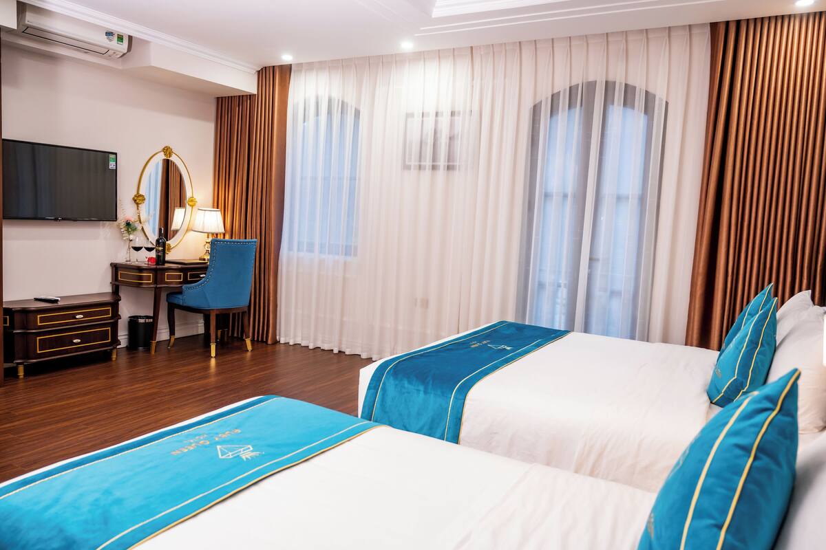 A hotel room with two beds, a desk with a chair, a TV, and curtains.