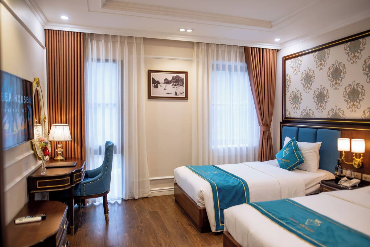 A hotel room with two beds, a desk, a chair, a TV, and a framed picture on the wall.
