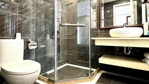 A modern bathroom with a glass-enclosed shower, a white toilet, and a vanity with a mirror. - Ruby Queen Hotel (Bai Chay)