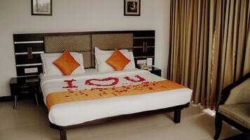 Een netjes opgemaakt bed met een wit-oranje sprei, twee kussens en een decoratief hart van rozenblaadjes dat ‘YOU’ spelt.