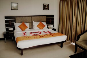 Una cama bien hecha con una colcha blanca y naranja, dos almohadas y un corazón decorativo hecho de pétalos de rosa que deletrea 'YOU'.
