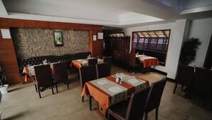 A restaurant with multiple tables and booths, stone walls, and a large window with a view. - Joance Regency (Thodupuzha)