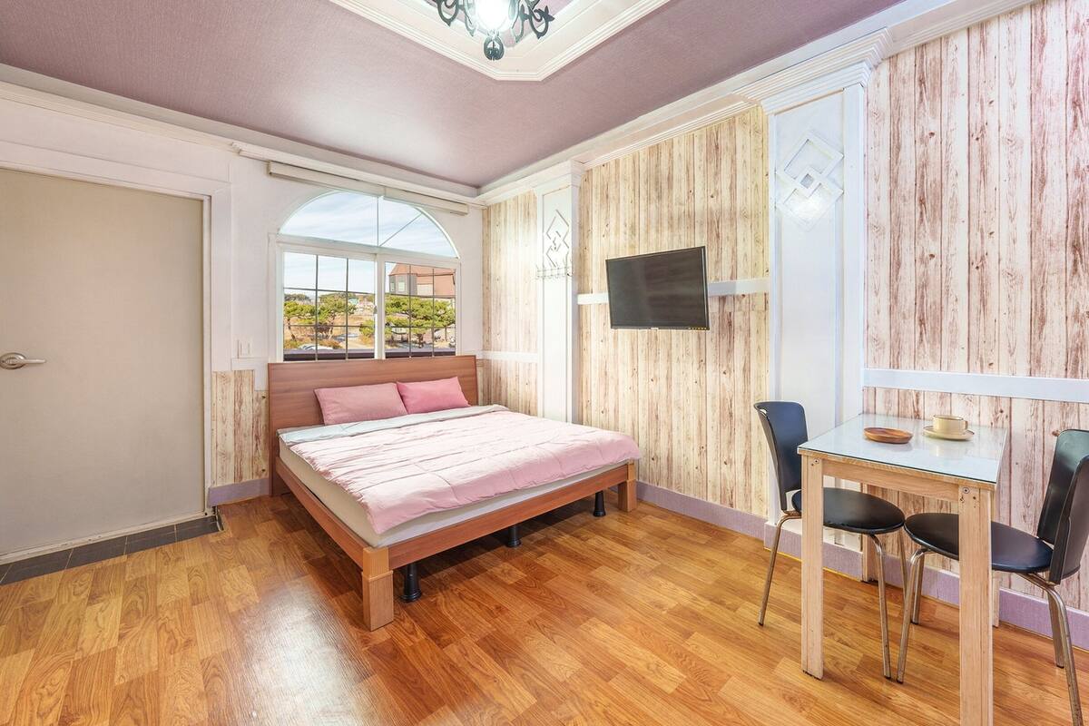Un dormitorio con cama, televisión, mesa y sillas, y ventana con vistas.