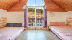 Un dormitorio con dos camas, una ventana grande con vistas a una valla y árboles, y techo de madera.