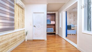 Un pasillo con piso de madera, una puerta blanca y un armario con ropa doblada.