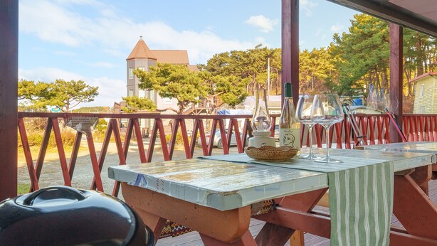 Una terraza de madera con una mesa lista para comer, con vistas a un paisaje de árboles y un edificio con torre.