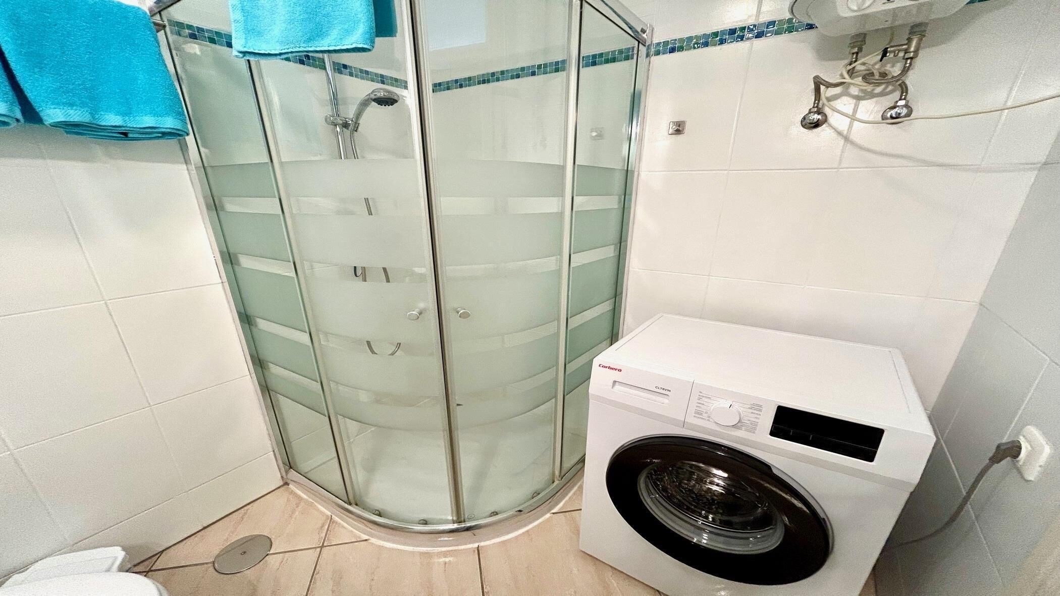 A small bathroom with a glass shower enclosure, a washing machine, and a toilet.
