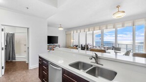 A modern kitchen with a large island, stainless steel sinks, and a view of the ocean.