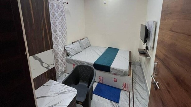 Une petite pièce, de taille modeste, comprenant un lit, une chaise, un bureau avec un ordinateur et un téléviseur.