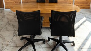 Un salón de conferencias con una mesa de madera y dos sillas de oficina negras, ventanas amplias con vistas y un cartel que indica una sala de relajación.