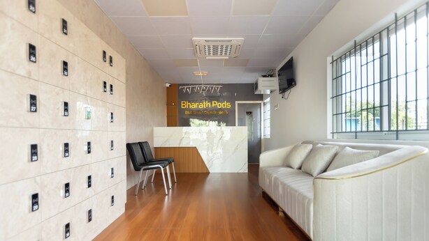 Un vestíbulo de hotel con mostrador de recepción, un sofá, una silla y una pared con taquillas numeradas.