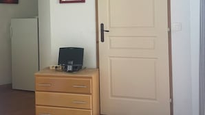 A room with a closed door, a mounted television, a mirror, a wooden dresser, and a white refrigerator. - Hameau 3 103 - SPA & Piscine Appartement 6 Pers (Orelle)