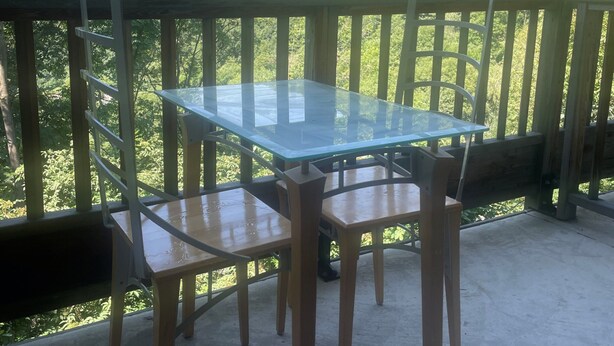 A glass-top table with wooden chairs on a balcony with a view of a green hillside and power lines. - Hameau 3 103 - SPA & Piscine Appartement 6 Pers (Orelle)