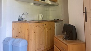 A compact kitchen with wooden cabinets, a microwave, a kettle, and a coffee machine. There are two trash bins and a small wooden cabinet with drawers. - Hameau 3 103 - SPA & Piscine Appartement 6 Pers (Orelle)