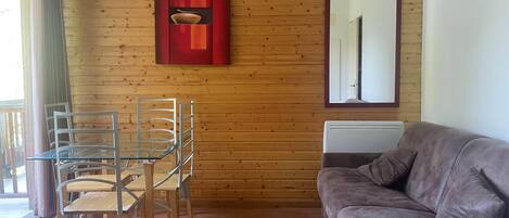 Una habitación con un revestimiento de madera en la pared, una mesa de vidrio con sillas, un sofá de cuero marrón y una obra de arte roja sobre la mesa.