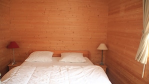 A wooden-paneled room with a bed, two bedside lamps, and a window with curtains. - Quiet Apartment in Nature (Chatel)