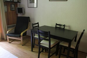 Ein Essbereich mit Tisch und vier Stühlen, einem Fernseher an der Wand und einem gerahmten Bild über dem Tisch.