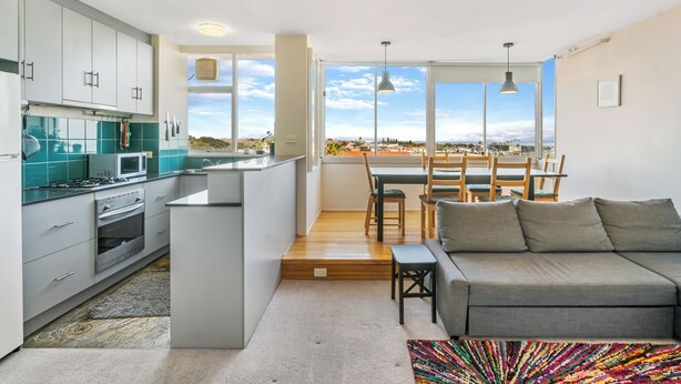 A modern kitchen with white cabinets, a built-in oven, and a large window overlooking a cityscape. - Marine Magic (St Kilda)