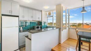 A modern kitchen with white cabinets, a teal backsplash, and a view of the city through large windows. - Marine Magic (St Kilda)