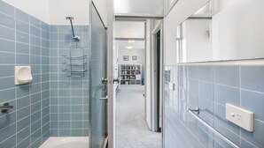 A modern bathroom with blue tiles, a glass shower enclosure, and a visible toilet paper holder. - Marine Magic (St Kilda)