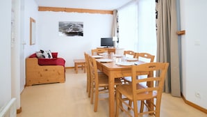 Una habitación con una mesa de comedor de madera para cuatro personas, un sofá rojo, una televisión y una ventana con cortinas.