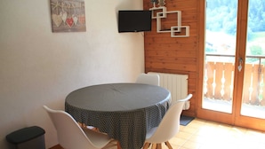 A round table with a polka dot tablecloth, two white chairs, a black speaker, a TV mounted on the wall, and a wooden door with a view of a fenced yard. - Voinettes Vnb8 Telecabine & Mountain 4 Pers (Chatel)