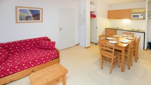 Un espacio habitable pequeño con un sofá rojo estampado floral, una mesa de comedor de madera para cuatro personas y un banco de madera.