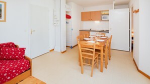 Un espacio habitable compacto con comedor, kitchenette y cama con ropa de cama estampada de flores rojas.