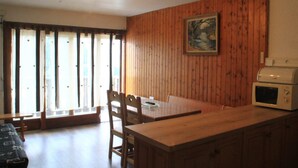 A wooden-paneled room with a dining table, chairs, a microwave, and a painting on the wall. - Tavaillons Tv31 Swimming Pool & Center 4 Pers (Chatel)