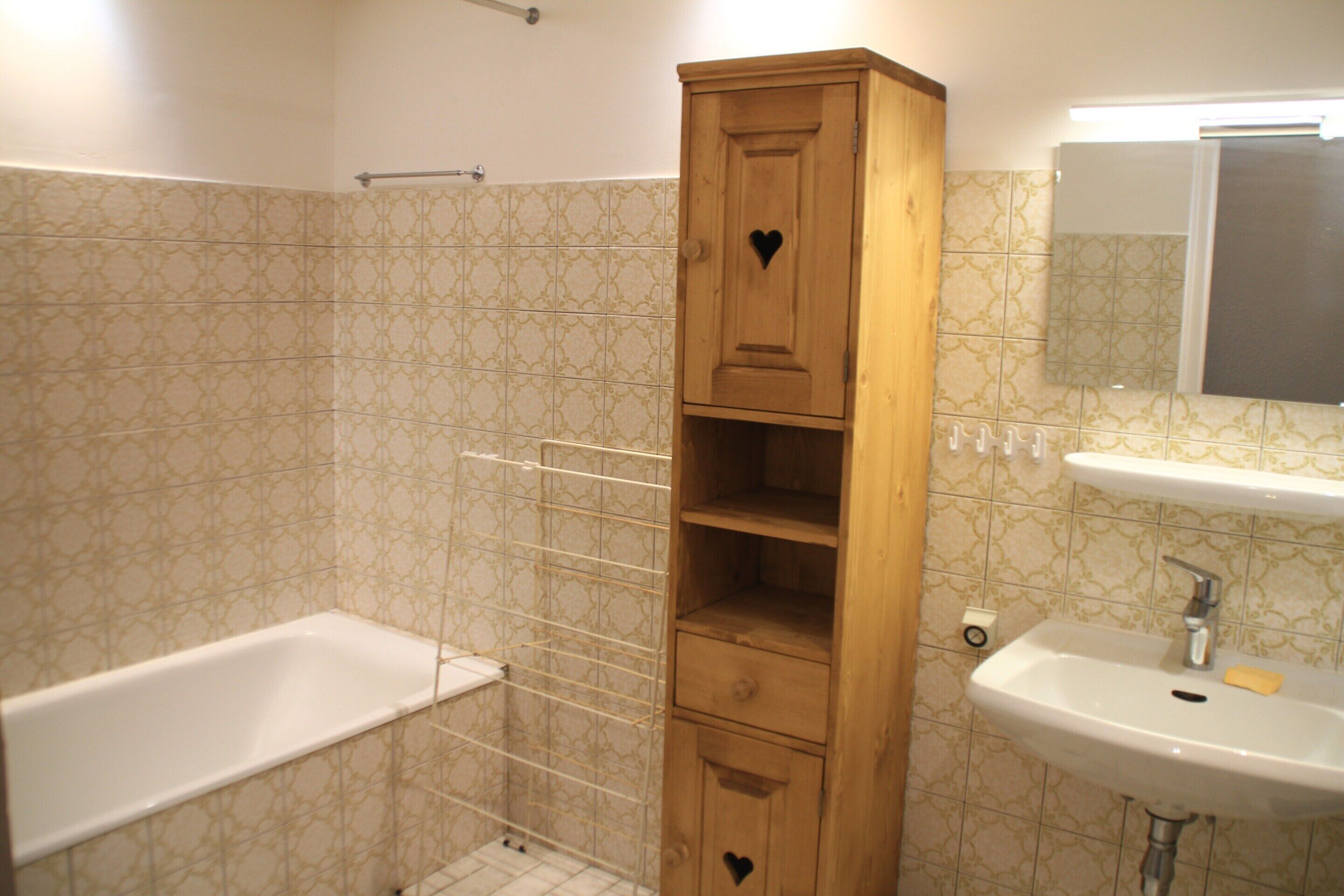 A bathroom with a wooden cabinet, a white bathtub, and a sink with a mirror above it.
