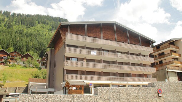 A multi-story hotel with balconies, a stone facade, and a view of a forested hillside. - Tavaillons Tv31 Swimming Pool & Center 4 Pers (Chatel)