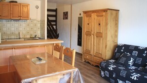 A compact living space with a dining table, wooden cabinets, a sofa, and a kitchen area with a tiled backsplash and wooden counter. - Tavaillons Tv31 Swimming Pool & Center 4 Pers (Chatel)