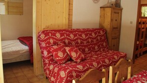 A room with a wooden bed, a red patterned sofa, and a wooden cabinet. - Voinettes Vnb2 Telecabine & Mountain 4 Pers (Chatel)
