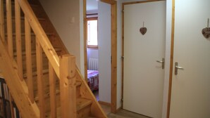 Un escalier en bois mène à une pièce où se trouve un lit et une porte ornée d’un motif en forme de cœur.