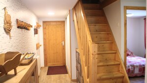 Un escalier en bois mène à une chambre à coucher où se trouvent un lit et un rideau rouge.