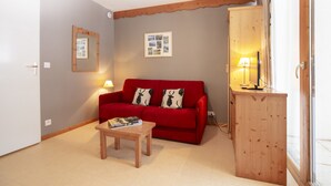 A room with a red sofa, a wooden table, a mirror, and a lamp. - Balcons C 001 - Parc Nat. Vanoise Appart. 5 Pers (Val-Cenis)