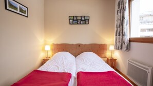 A double bed with red blankets, two bedside lamps, a wall-mounted photo collage, and a window with curtains. - Balcons C 001 - Parc Nat. Vanoise Appart. 5 Pers (Val-Cenis)