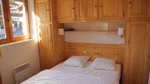 Un dormitorio con cabecera de madera, cama con ropa de cama blanca, una ventana y armarios de madera.