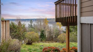 Une vue depuis un balcon donnant sur un lac, avec des arbres et une silhouette de ville en arrière-plan.