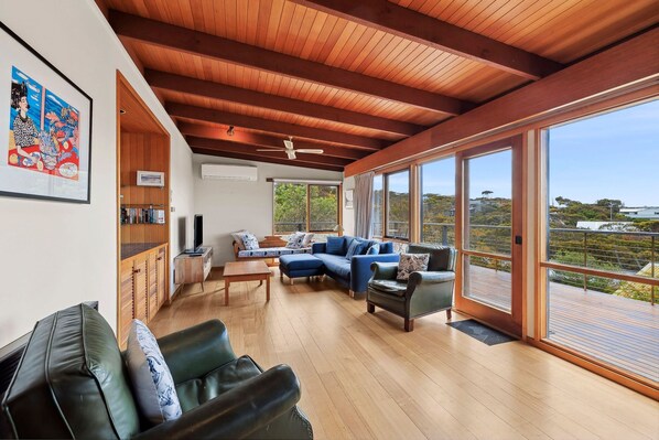 A spacious living area with a wooden ceiling, a large window offering a view of the outdoors, and a seating arrangement including a sofa and a chair.
