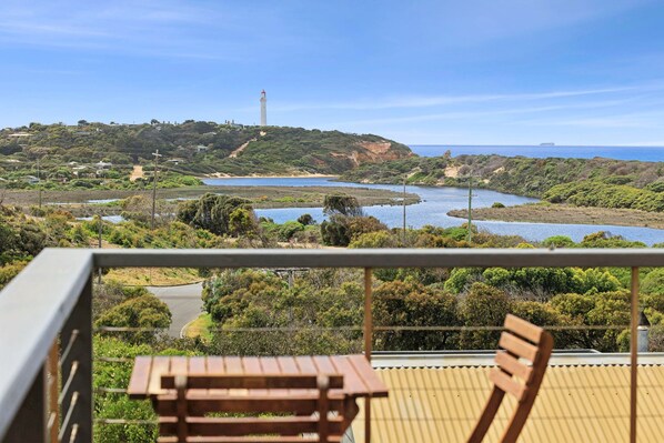 A balcony with a view of a coastal landscape, including a lighthouse, a river, and a hilly terrain. - Banksia Haven (Fairhaven)
