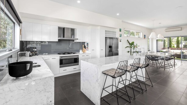 A modern kitchen with white cabinetry, a marble island, and a dining area with bar stools.
