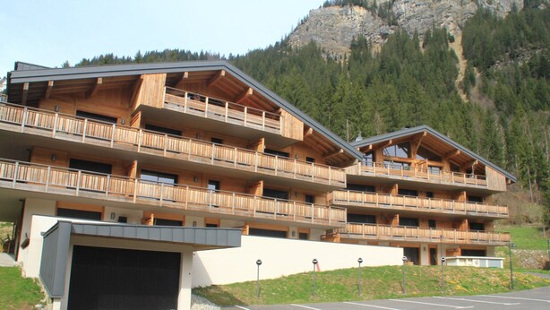 Un hotel a più piani con balconi, un garage e montagne sullo sfondo.