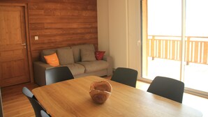 Un tavolo da pranzo in legno con sedie, una parete in legno, un divano con cuscini e una porta scorrevole in vetro che dà su uno spazio esterno.