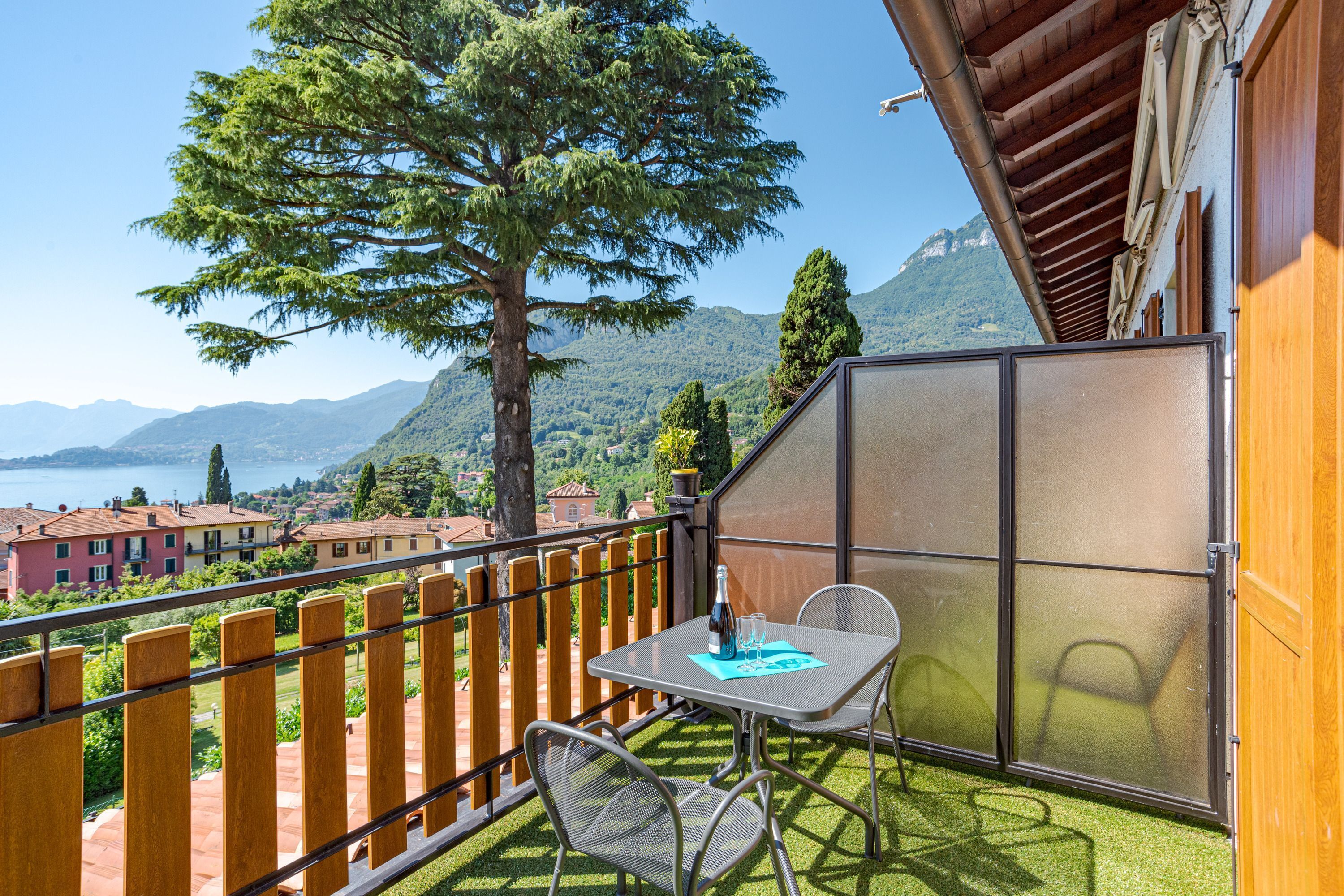A balcony with a table and chairs, overlooking a scenic mountain view and lake.